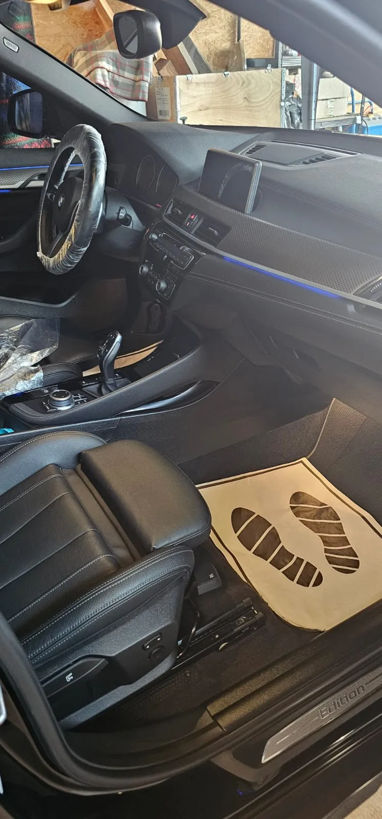 BMW-Innenraum während der Aufbereitung: Lenkrad in Schutzfolie und Einweg-Fußmatte im Fußraum